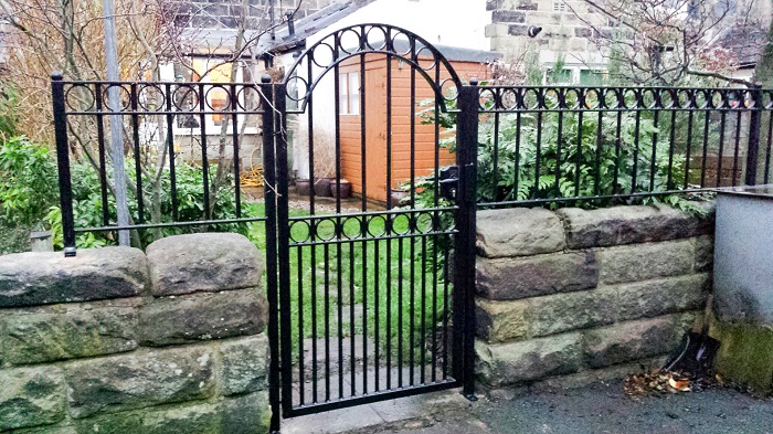 A short and small metal gate with rocky stone walls for a backyard garden.