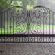 Ornamental metal driveway gates in a tranquil green environment.