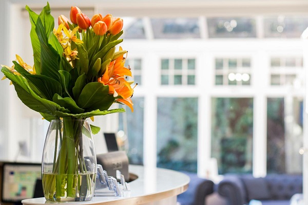 A glass vase filled with pleasant orange flowers opplaced on a dental clinic reception desk table. 