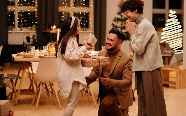 A girl is getting gifts from two persons at the home.